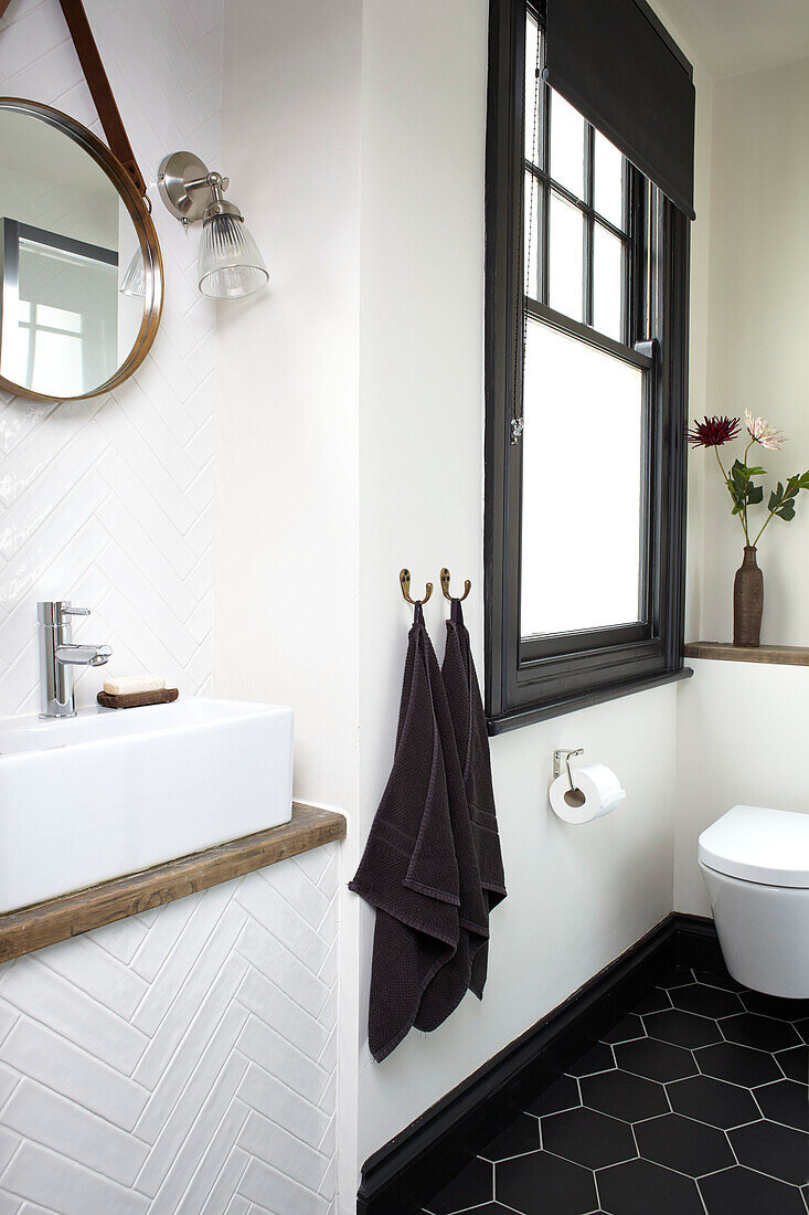 Schwarze Handtücher hängen am Milchglasfenster mit rundem Spiegel über dem Waschbecken im Badezimmer eines Hauses in Brighton, East Sussex, UK