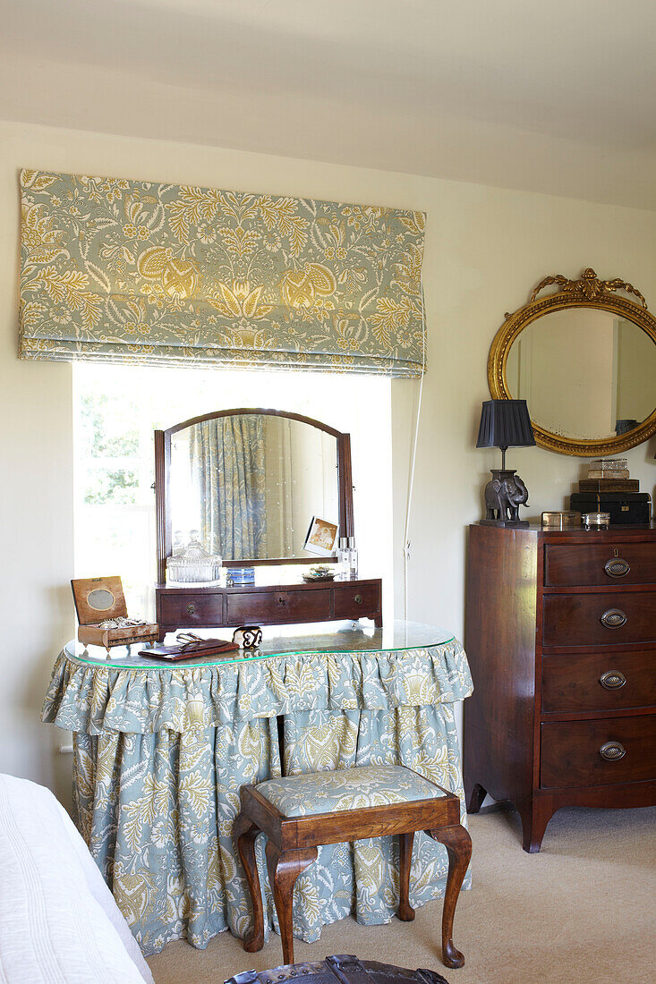 Ovaler vergoldeter Spiegel über einer Holzkommode in einem Schlafzimmer in Wiltshire mit passenden Stoffen, England, UK