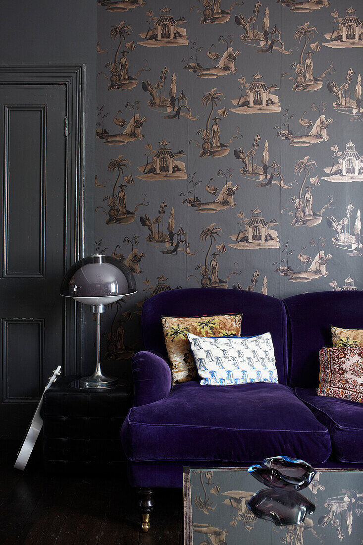 Vintage-Lampe mit lila Sofa und gemusterter Tapete in einem Londoner Wohnzimmer im Retrostil, England, UK