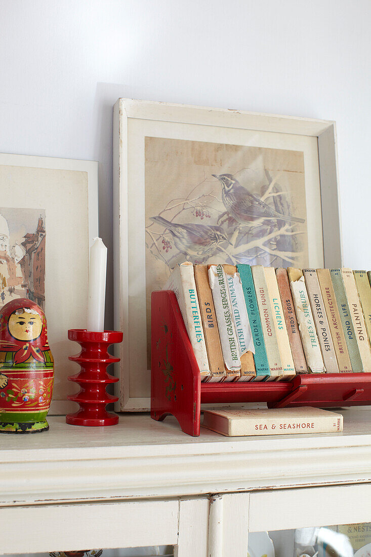 Vintage-Bücher und Kunstwerke mit Kerze und russischer Puppe auf einem Schrank im Wohnzimmer in Ryde, Isle of Wight, UK