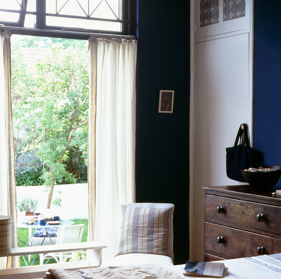 Ecke des blau-weißen Schlafzimmers mit Blick auf Tisch und Stühle im Garten
