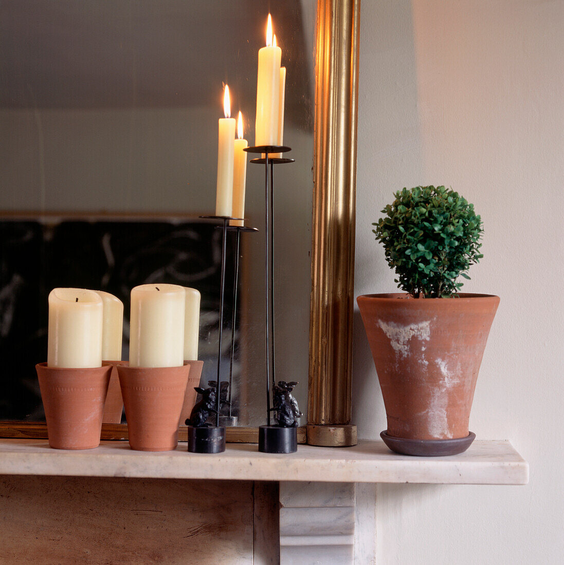 Terrakotta-Töpfe und Kerzen auf einem Marmormantel mit vergoldetem Spiegel