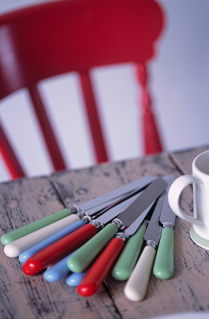 Colourful fifties style cutlery on wooden table with red chair