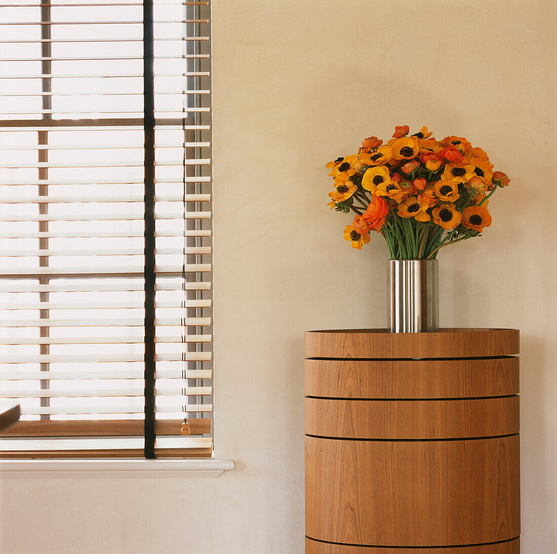 Window with venetian blinds and metallic vase with orange Anemone flowers