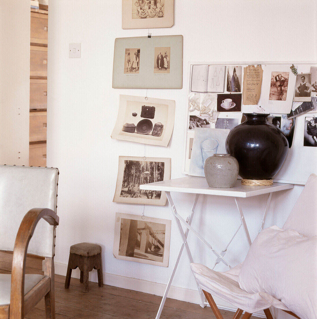Display of black and white photographs and postcards on a wall beside a folding table with pots