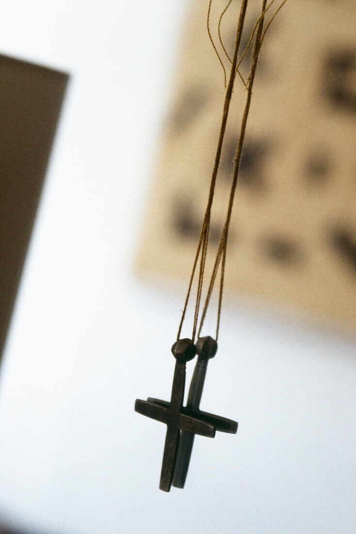 Metallic cross pendant on a string cord hanging against a mirror