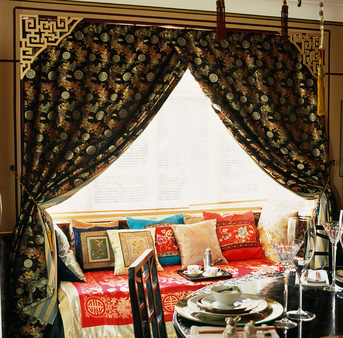 Esszimmer mit gedecktem Tisch und dramatischer Fensterfront, die mit chinesischen Seidenkissen und Stoffen bedeckt ist