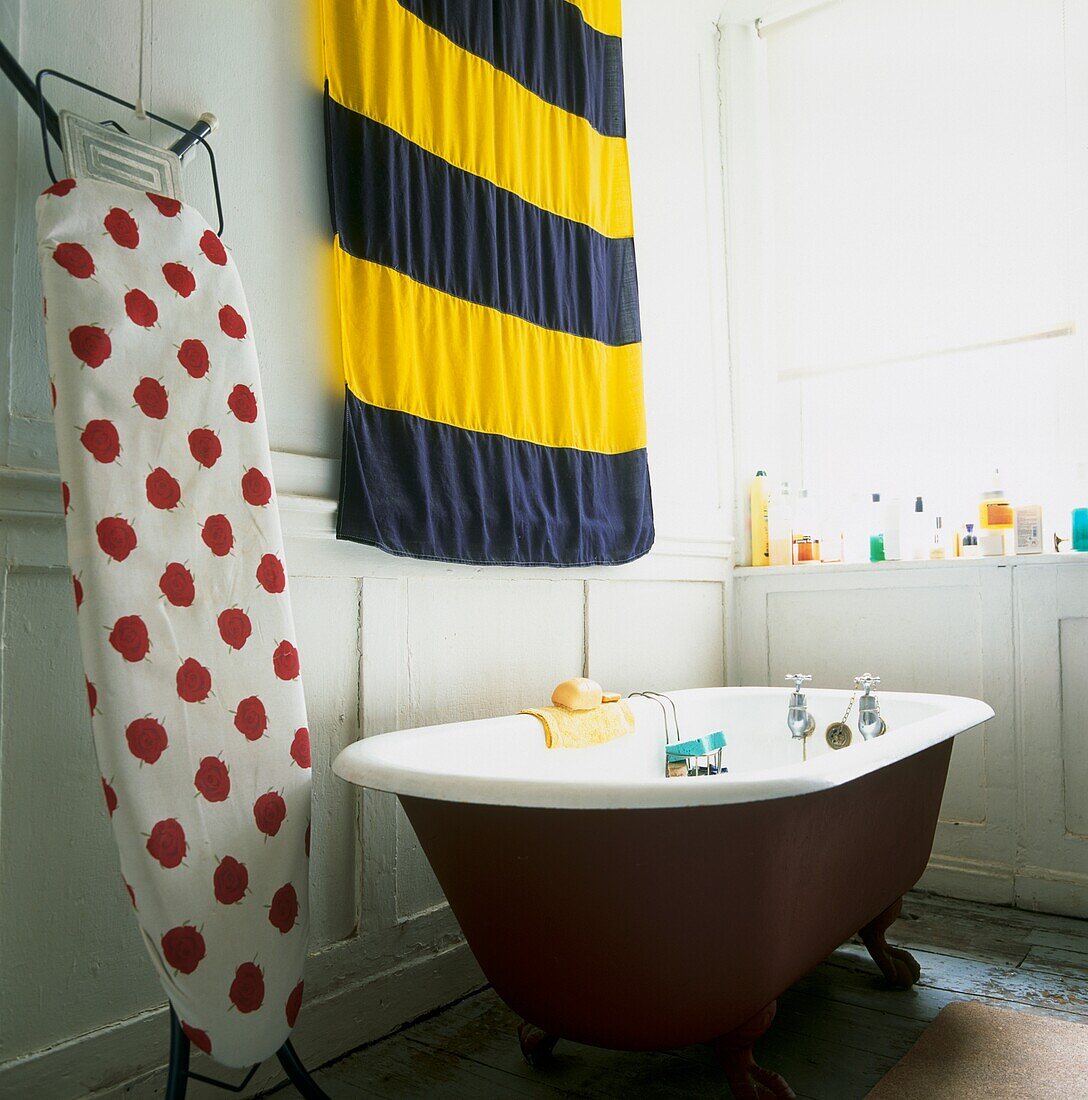 Pop-Art-Stillleben mit rot-weiß gepunktetem Bügelbrett und Signalflagge in einem weiß getäfelten Badezimmer mit Roll-Top-Badewanne