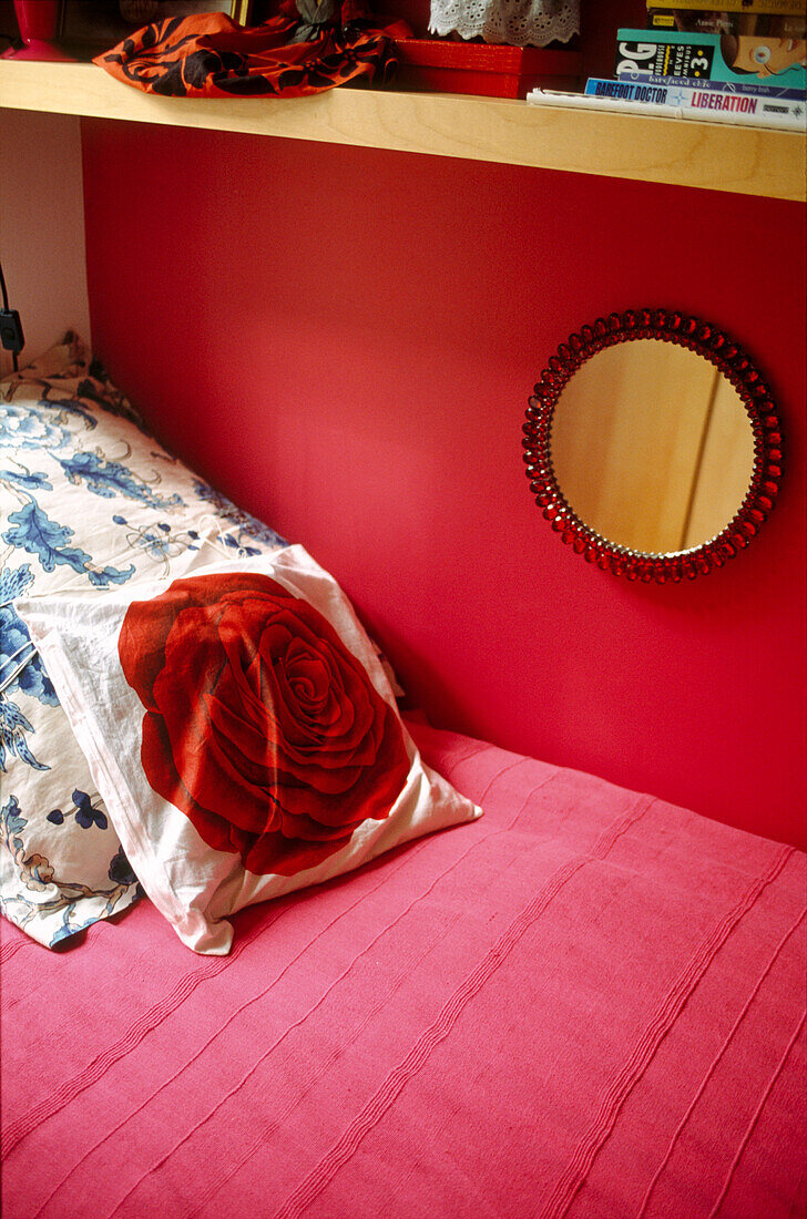 Magentarotfarbenes Jugendzimmer mit Streukissen mit Rosendruck und Wandregal mit Unordnung
