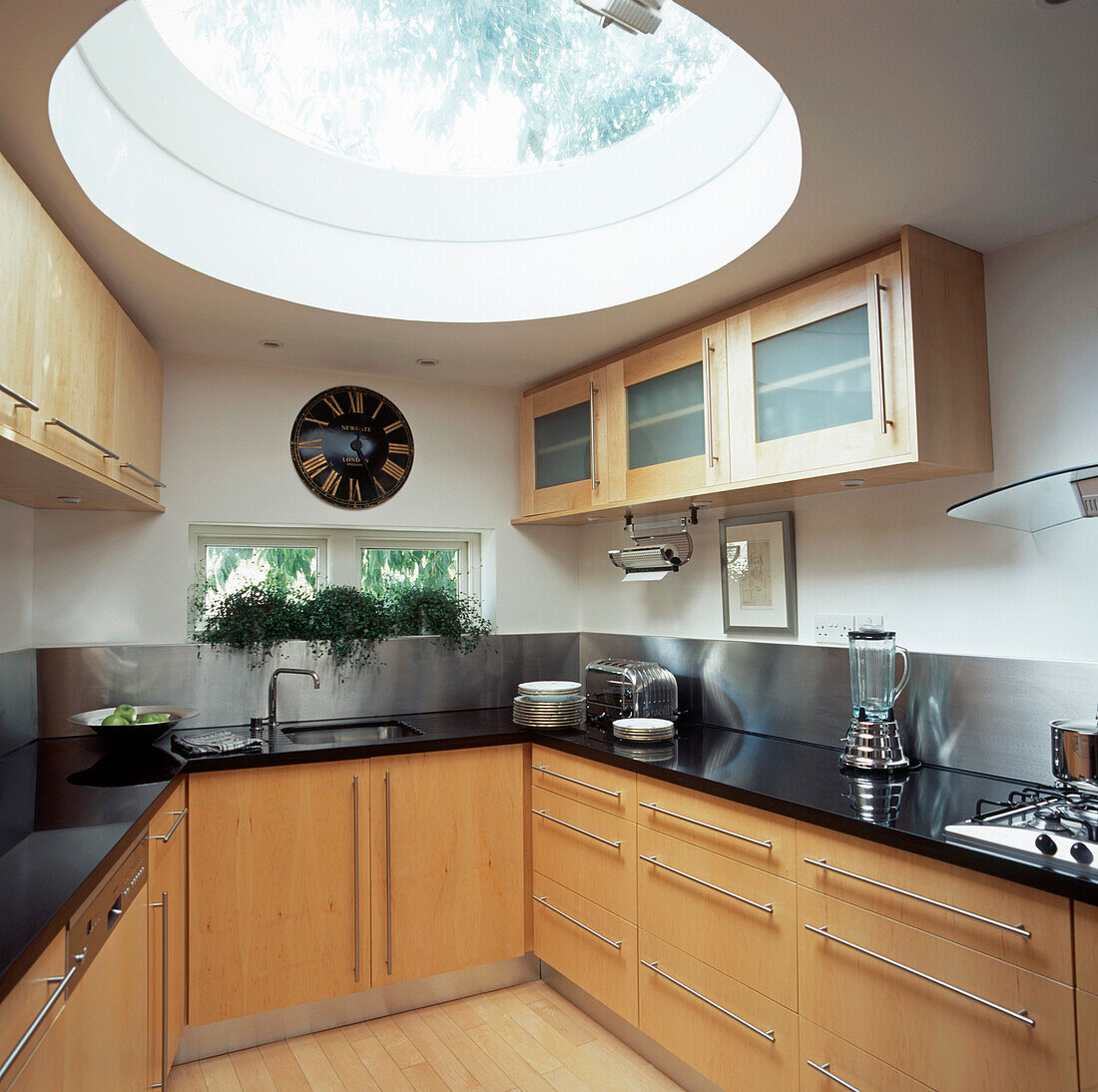 Abgewinkelte Küche mit kuppelförmigem Glasdach, Arbeitsplatten aus schwarzem Granit, Holzschränken und Spritzschutz aus Edelstahl