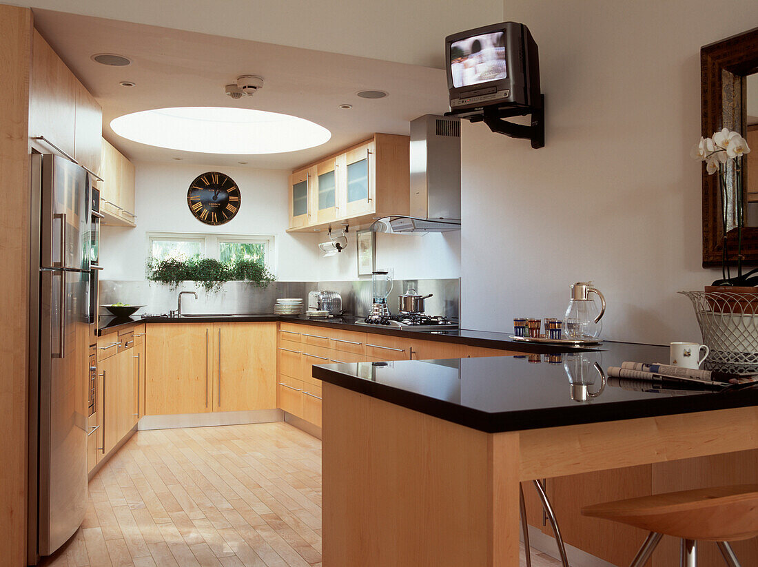Zeitgenössische erweiterte Küche mit schwarzen Granit-Arbeitsplatten, hellen Holzschränken, hellen Holzböden und einem runden Deckenfenster