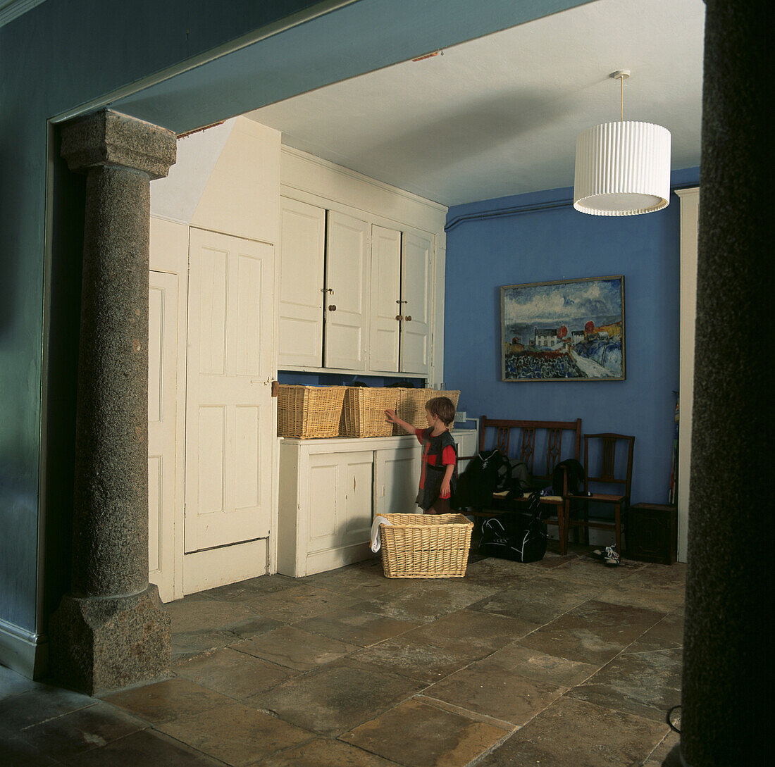 Young child in laundry room with fitted cupboards and wicker baskets