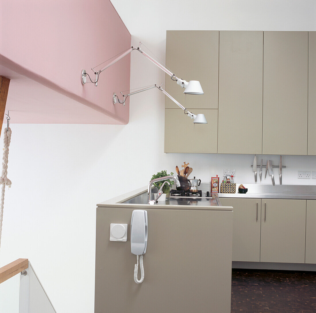 Moderne Küche mit freitragenden Wandleuchten aus Aluminium an einer auffallend rosafarbenen Wand über einer Arbeitsplatte aus Edelstahl auf grauen Einbauschränken