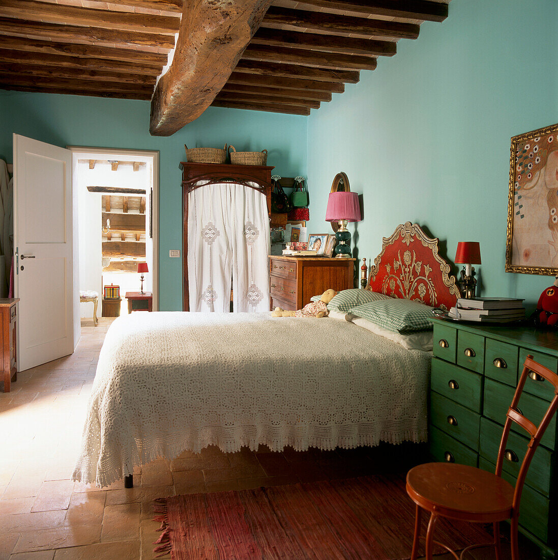 Hauptschlafzimmer mit zartblau gestrichenem Bett, das mit einer hübschen Spitzendecke und einem goldfarbenen und roten dekorativen Barockkopfteil versehen ist