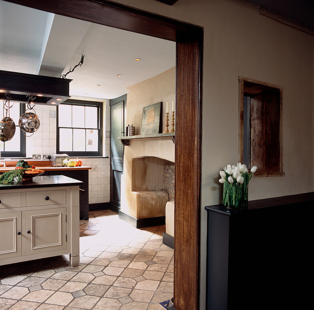 View from corridor of traditional kitchen in London town house with free standing furniture and stone fireplace