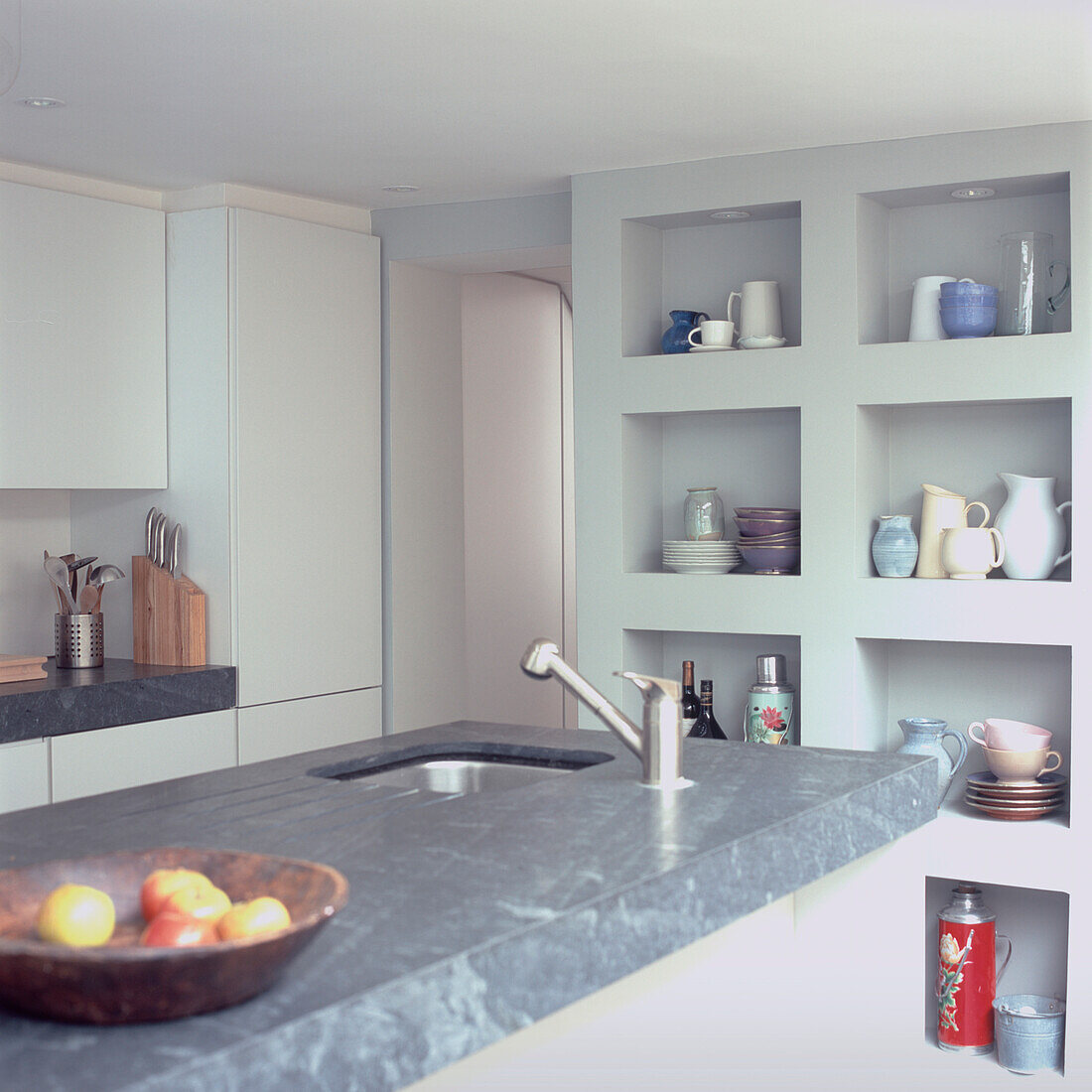 Kitchen island in grey marble effect plastic laminate and boxed in shelves in modern white kitchen