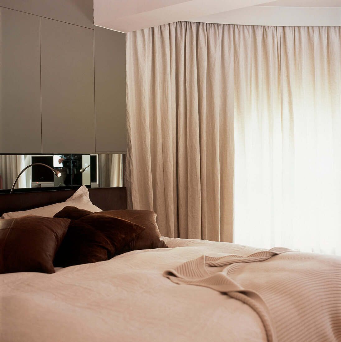 Schlafzimmerdetail mit Deckenkissen und Spiegel mit Leinenvorhängen in voller Länge