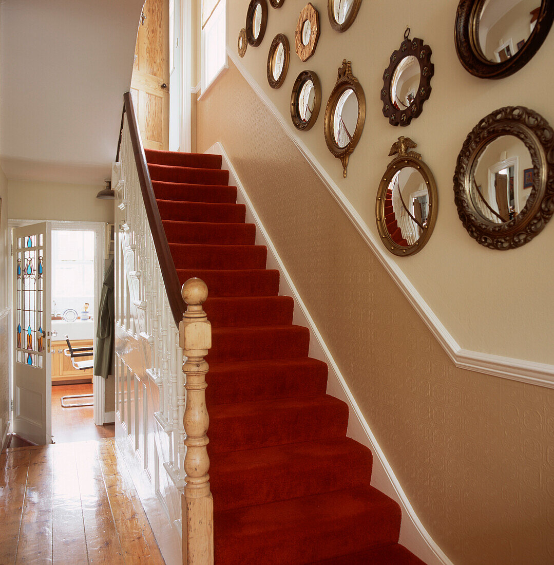 Treppe und Treppenabsatz im Erdgeschoss mit rotem Teppich auf der Treppe, Holzböden, zweifarbig gestrichenen Wänden und Sockelleiste