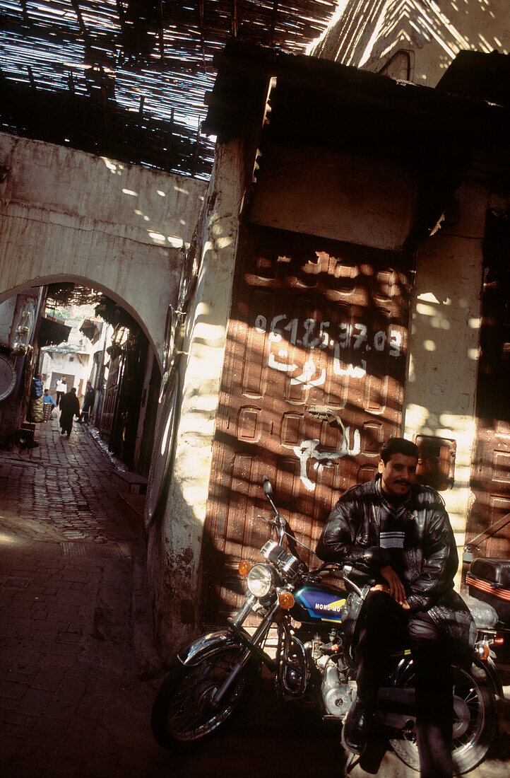 Mann auf seinem Motorrad sitzend im gedämpften Sonnenlicht in einer überdachten Gasse in der Medina von Fez, Marokko
