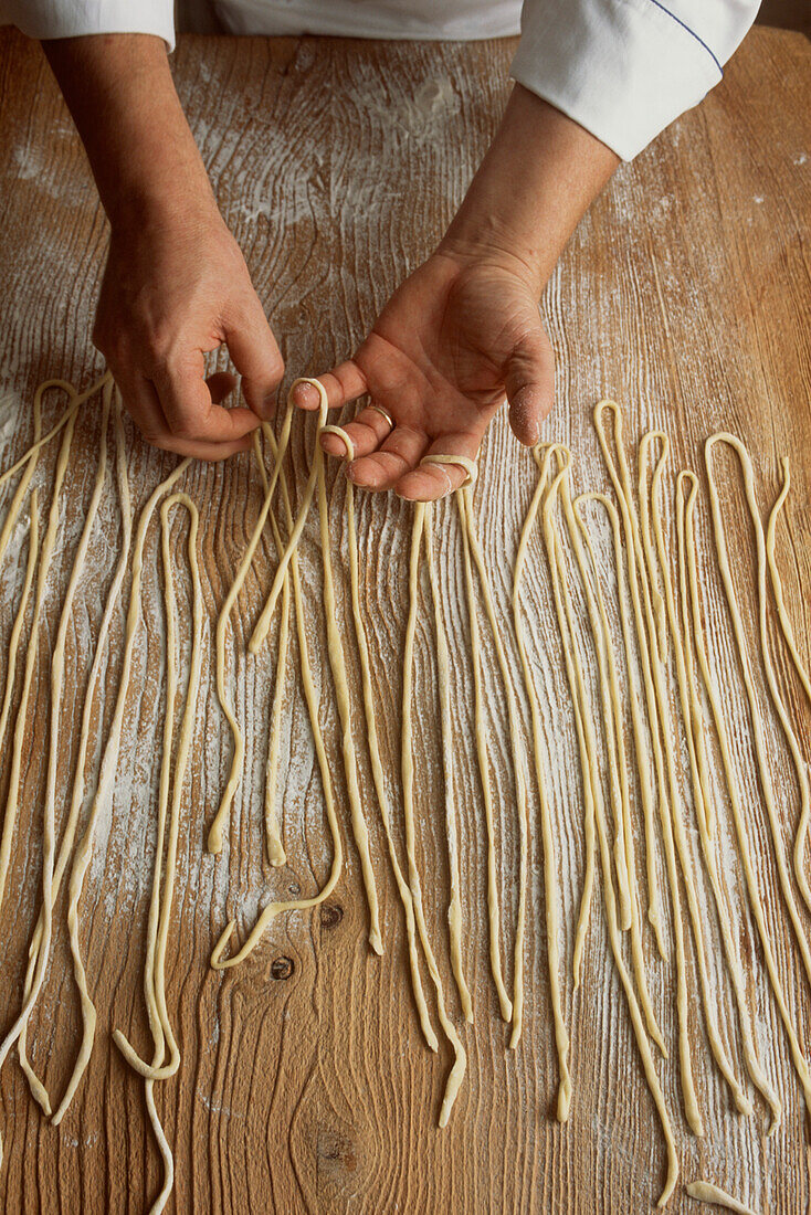 Köche bereiten mit ihren Händen frisch zubereitete Nudeln auf einer bemehlten Küchenarbeitsfläche zu