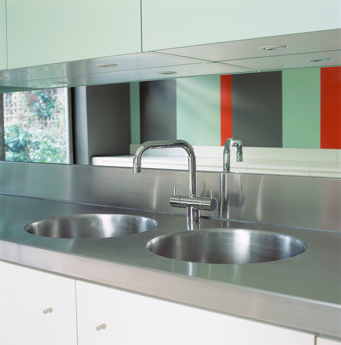 Mirrored splash-back with reflections of striped wall behind stainless steel worktop with double sink 