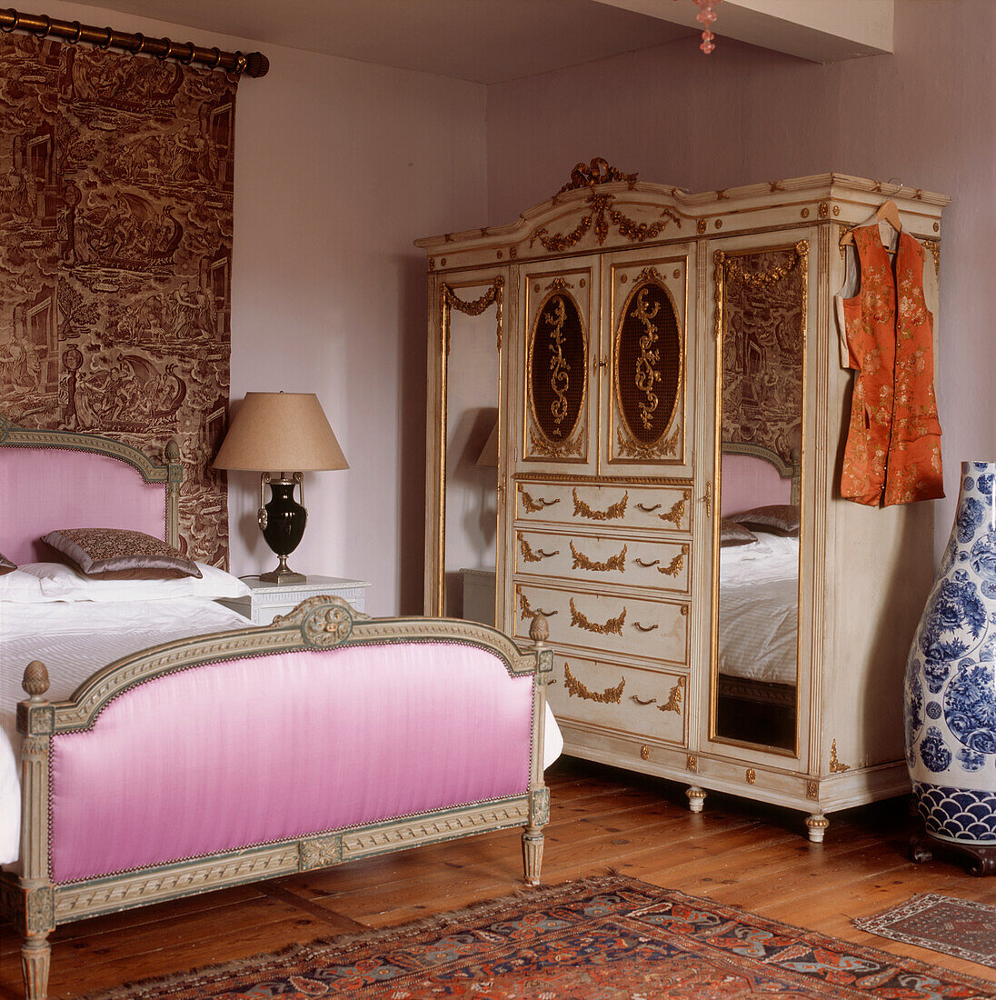 Ornate French period style bedroom with pink velvet fabric covered bedstead and decorative gold leaf wardrobe
