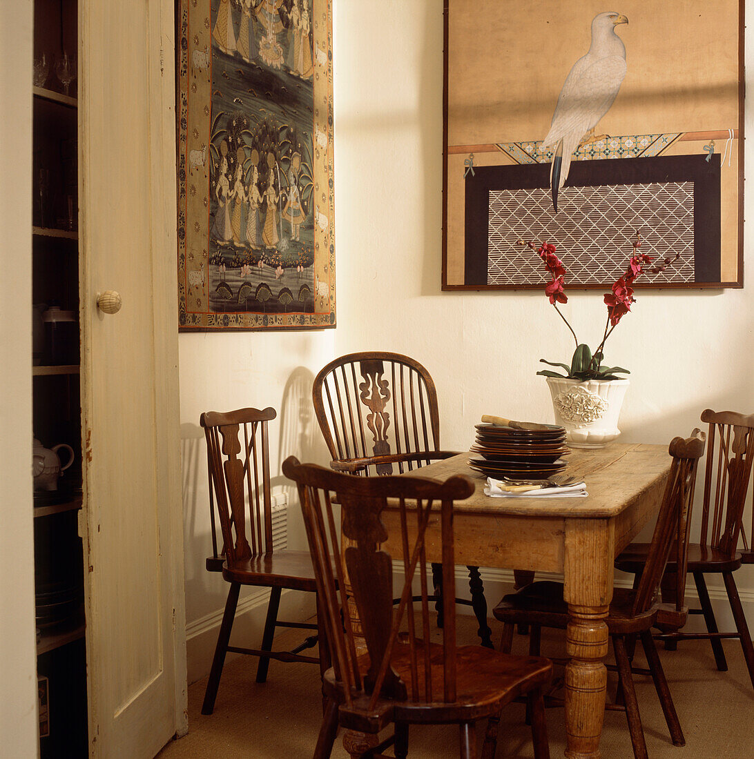 Küche mit Esstisch aus Kiefernholz und großen chinesischen Drucken an der Wand, verschiedenen antiken Esszimmerstühlen mit Spindellehne und einer roten Orchidee im Topf