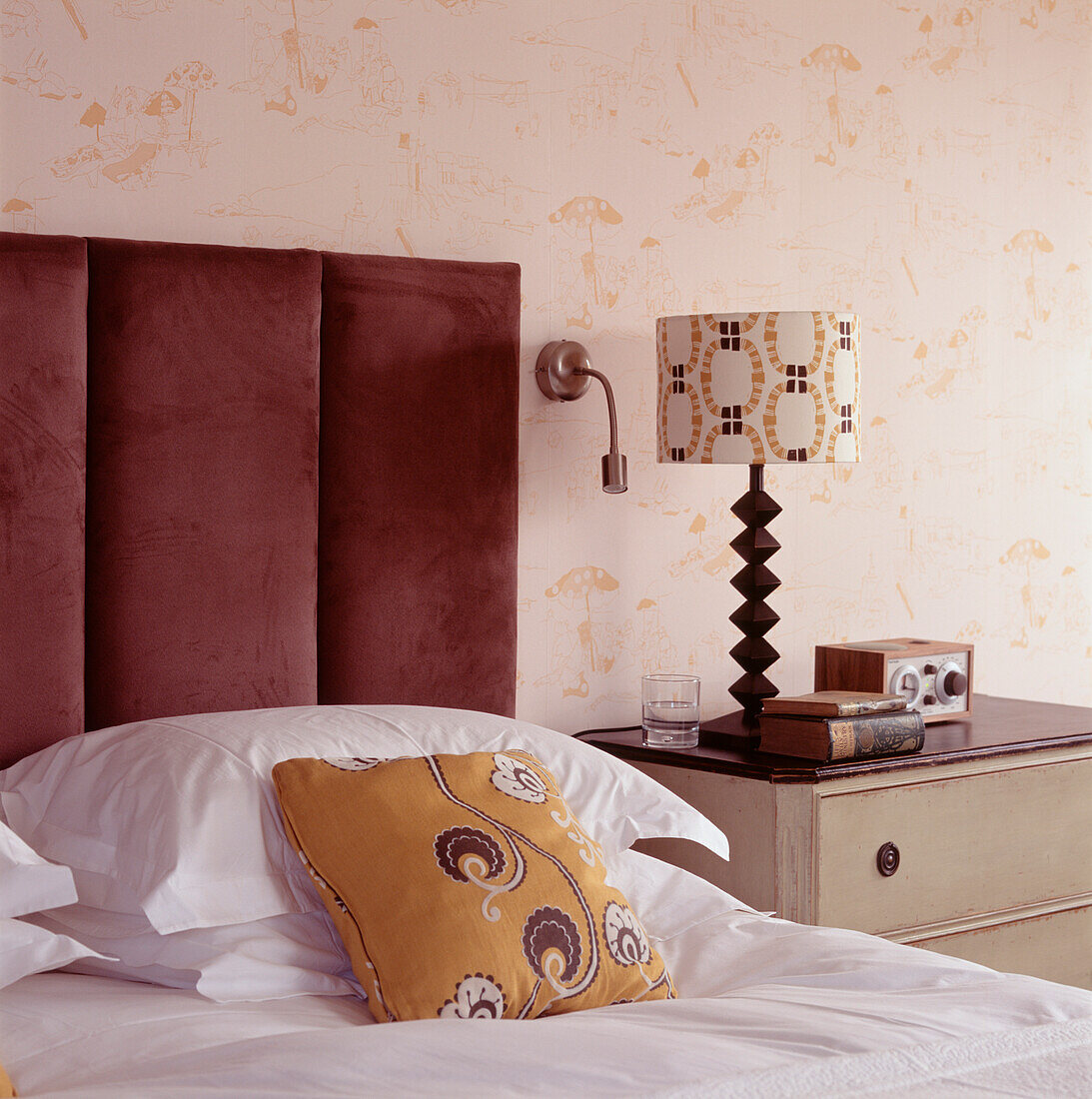 Schlafzimmerdetail mit gepolstertem Kopfteil aus Wildleder und gemusterten Einrichtungsgegenständen