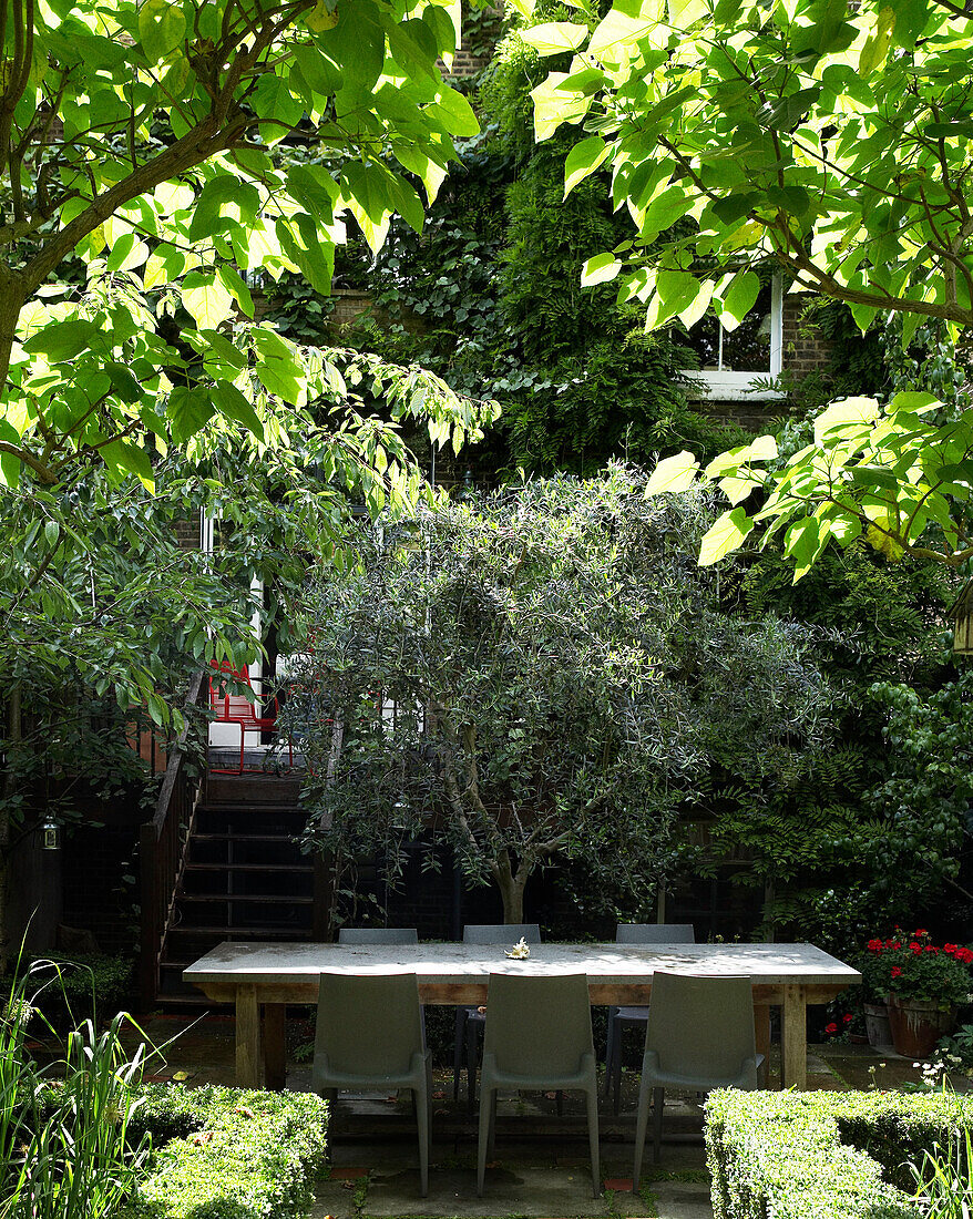 Üppiger grüner Garten mit Terrasse und großem Tisch und Stühlen