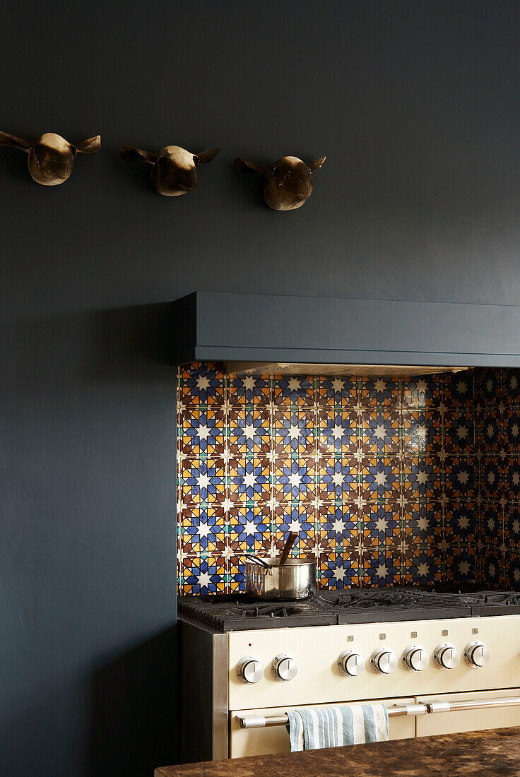 Detail of kitchen stove with Moorish wall tiles and sheep's head sculptures on a dark painted wall