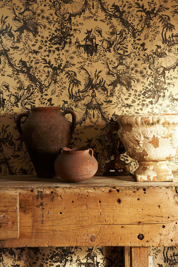 Detail of collection of vintage pottery on an old workbench in front of Chinoiserie wallpaper