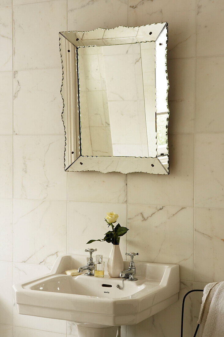 Waschbecken im Badezimmer mit Marmorwandfliesen und venezianischem Spiegel
