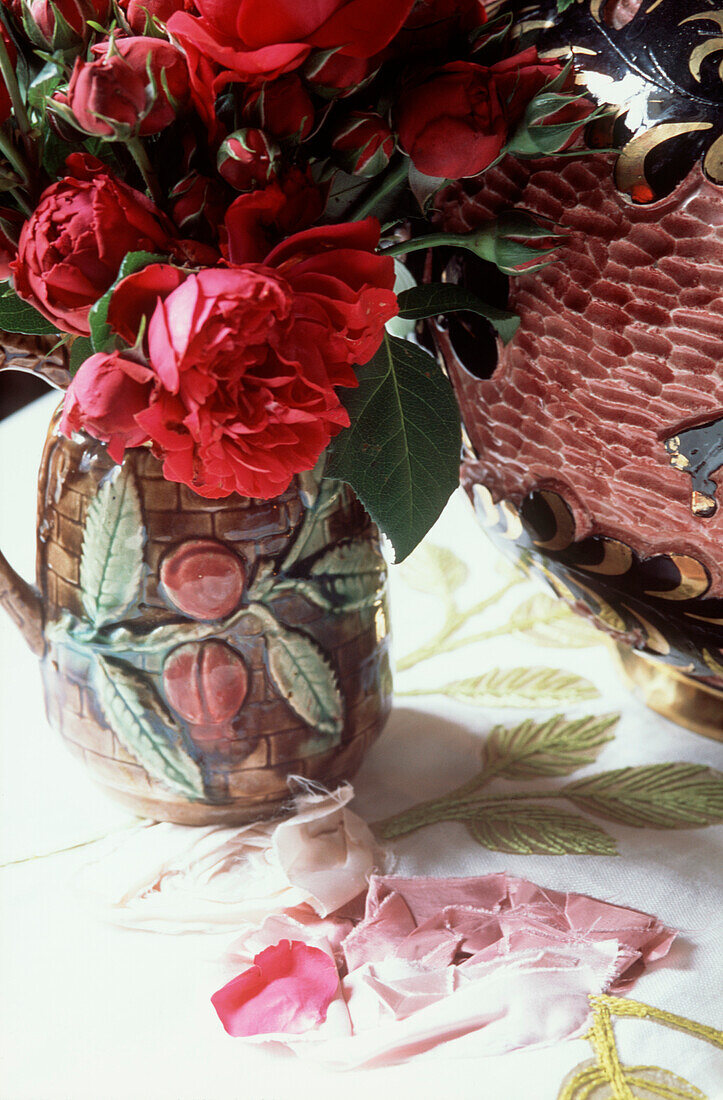 Detail eines farbenfrohen roten Blumenbouquets in einer Keramikvase auf einem blumenbestickten Tischtuch
