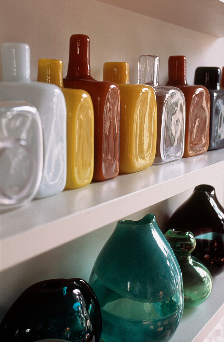 Detail von offenen Regalen mit einer Sammlung von bunten modernen Glaswaren, Vasen und Flaschen