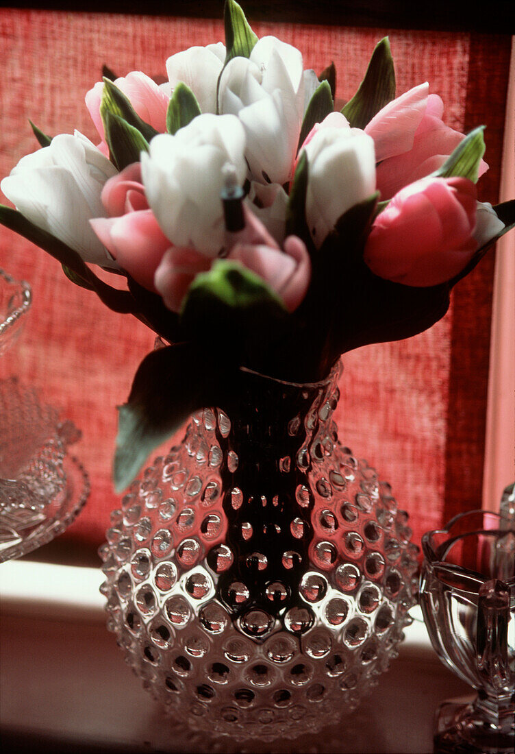 Gepunktete Vase aus klarem Glas, gefüllt mit einem Strauß rosa und weißer Tulpenblüten