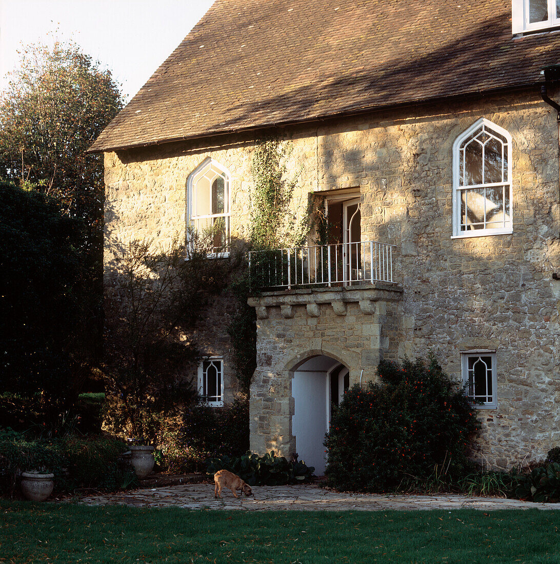 Außenansicht eines historischen Landhauses mit Rundbogenfenstern und -tür und Steinmauern