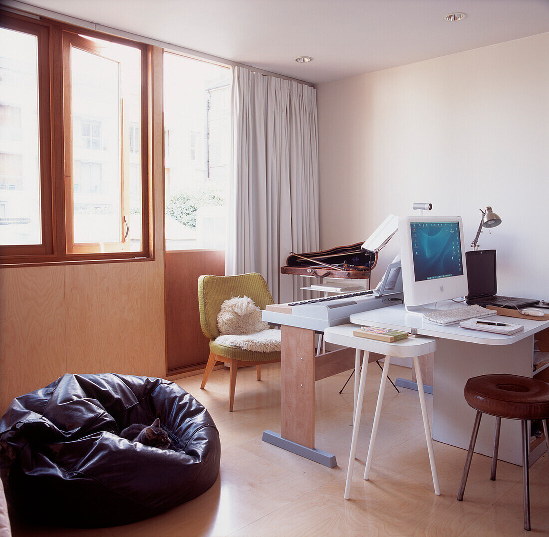 Zeitgenössisches Heimbüro mit großen Fenstern und lackiertem Holzfußboden, Schreibtisch, Computer und Musikinstrumenten