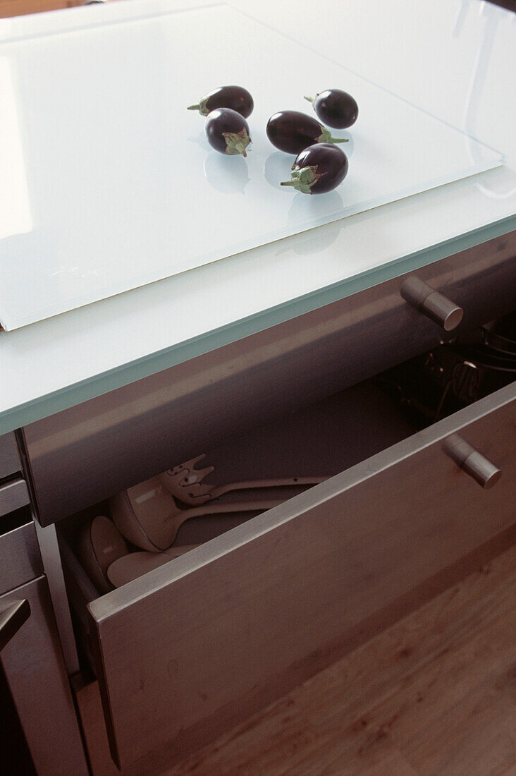 Gruppe kleiner Auberginen auf Glasarbeitsplatte in moderner Küche mit Edelstahlschubladen