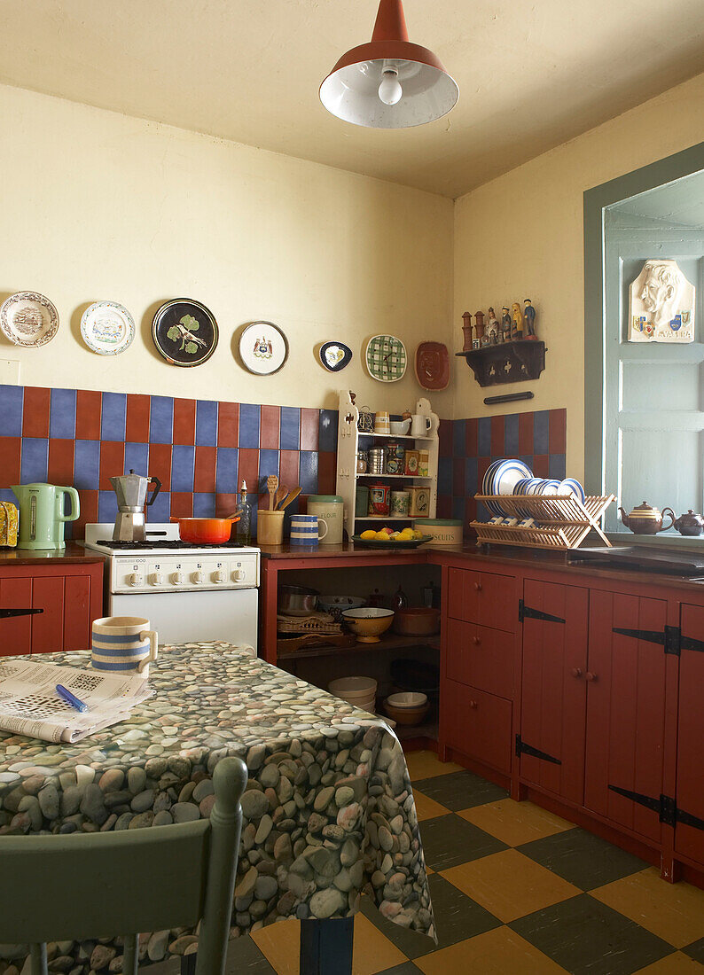 kitchen with red painted cupboards and vintage plates on the wall above red and blue wall tiles