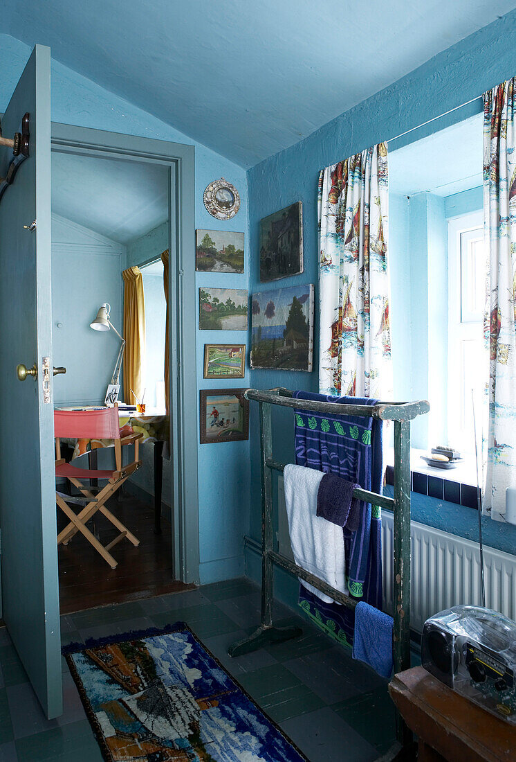 Ein hellblaues Badezimmer ist zu einer Galerie mit naiven Landschafts- und nautischen Gemälden geworden