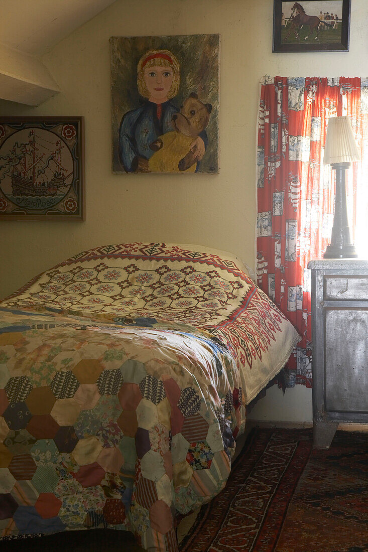 Eine alte Patchworkdecke und alte Stoffe schmücken das Schlafzimmer, darüber hängen naive Gemälde