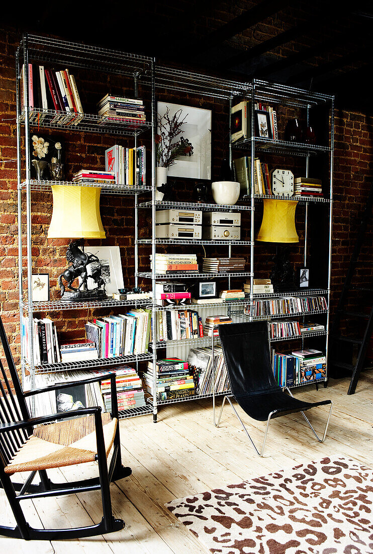 Großes Metallregal mit Büchern, CDs und Objekten vor freiliegender Ziegelwand im Wohnzimmer