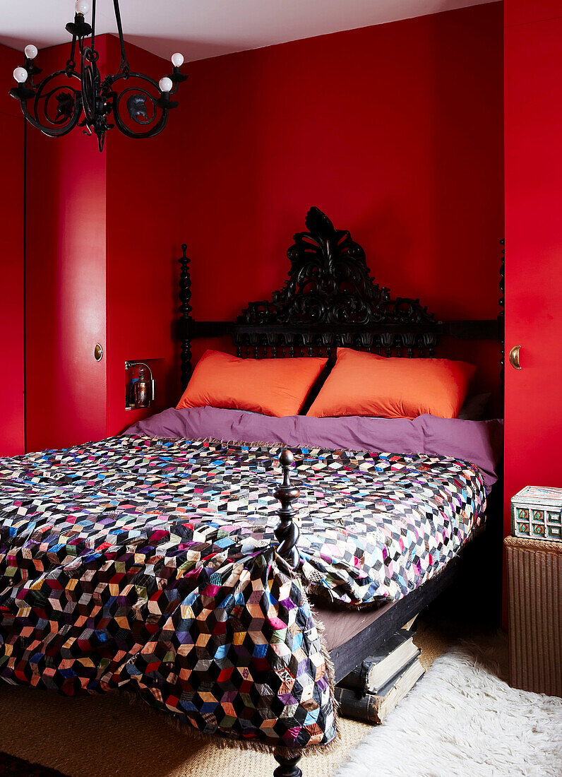 Farbenfrohes rotes Schlafzimmer mit mehrfarbiger Tagesdecke und dekorativem Bettkopfteil und Kronleuchter
