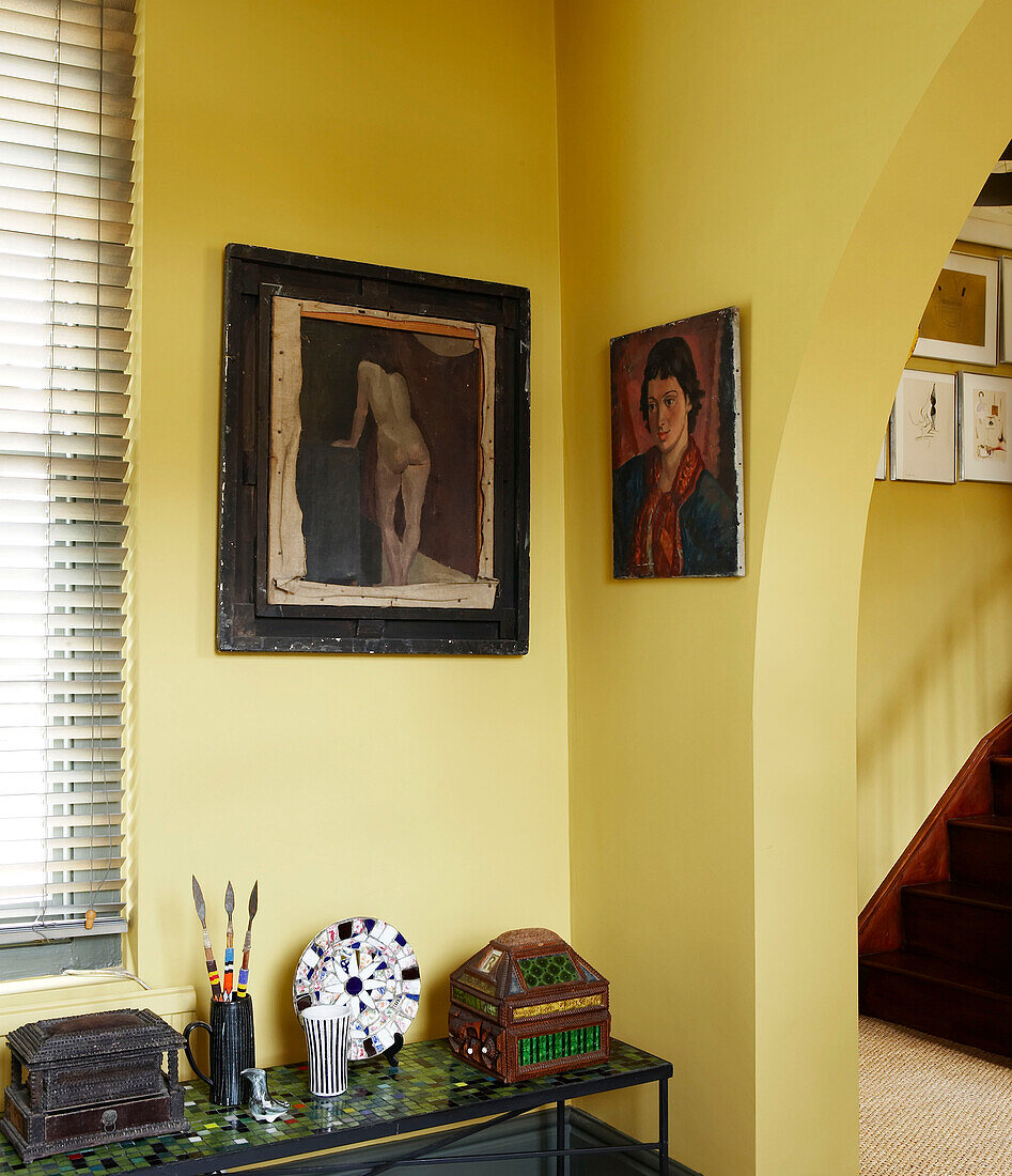 Nahaufnahme einer Zimmerecke mit gelber Wand und alten Gemälden im Flur