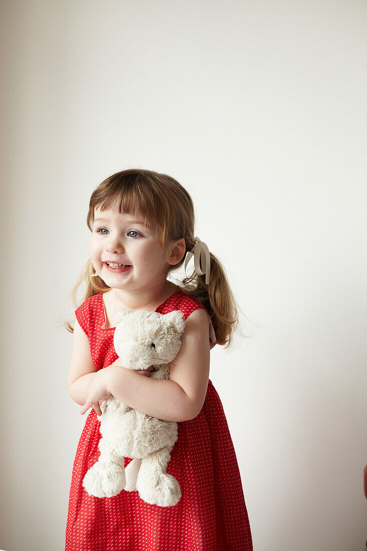 Junges Mädchen in rotem Kleid mit Teddybär in der Hand