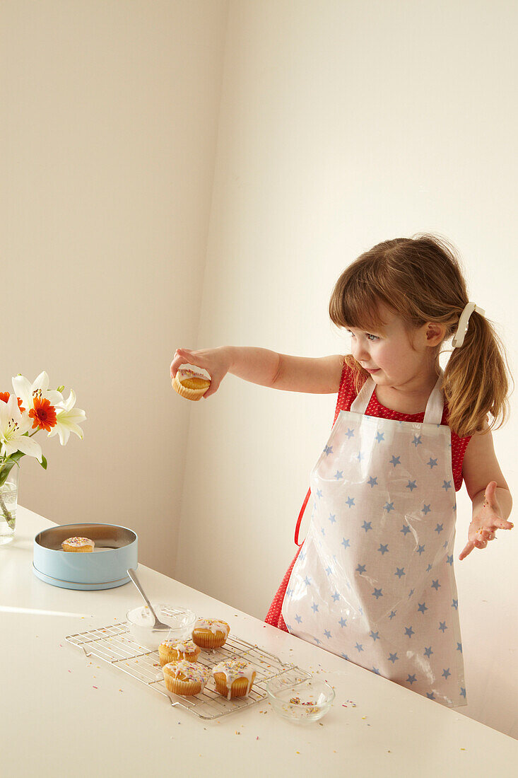 Drei Jahre altes Mädchen steht am Abkühlgitter und hält einen Fairy cake in der Hand