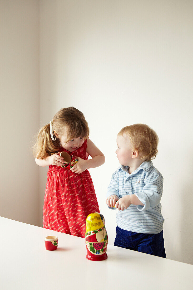 Junges Mädchen in rotem Kleid zeigt ihrem Bruder eine russische Puppe