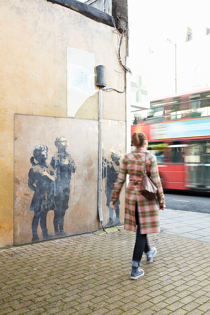 Woman walking past landmark graffiti in London city street, UK