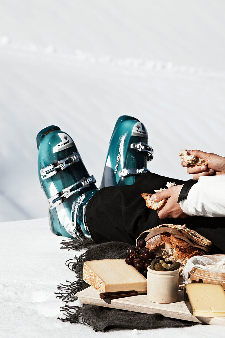 Mann in Skistiefeln sitzt und isst Brot und Käse in Zermatt, Schweiz