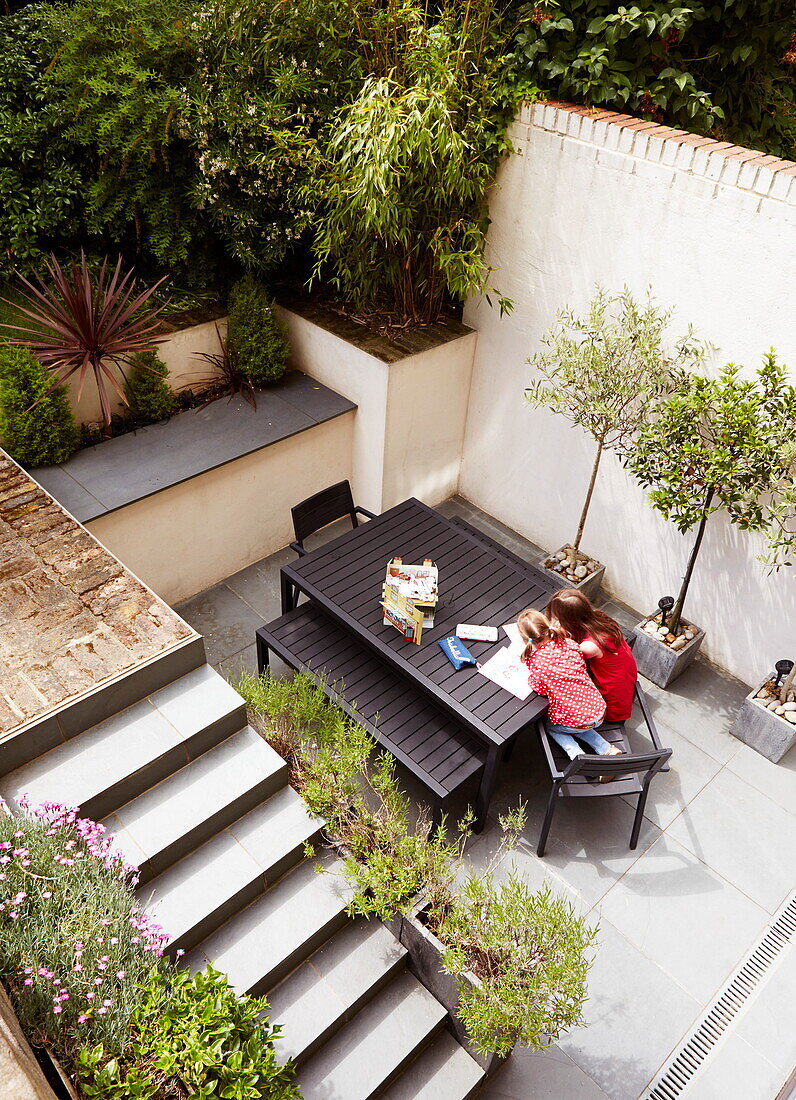 Elevated view of two girls sitting in terrace courtyard at table, London, England, UK